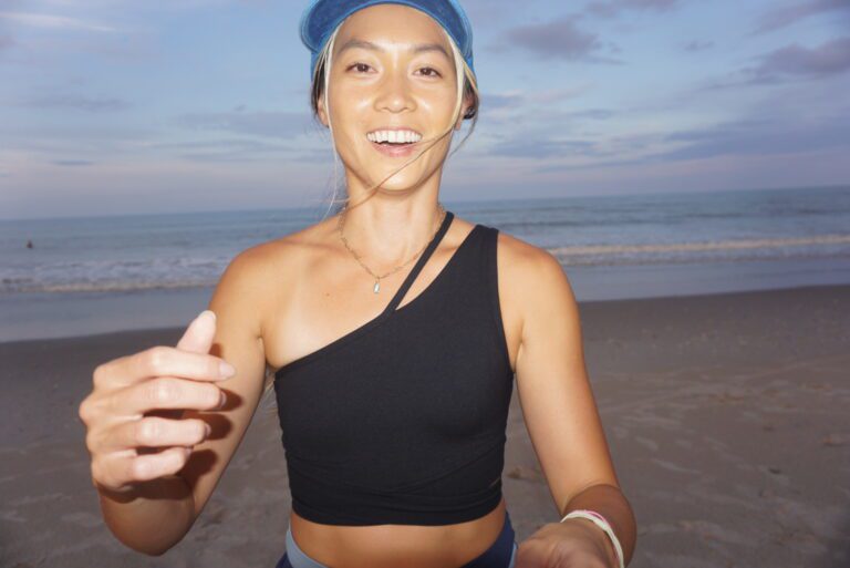 Woman smiling in black activewear at the beach — coastal living in your 30s
