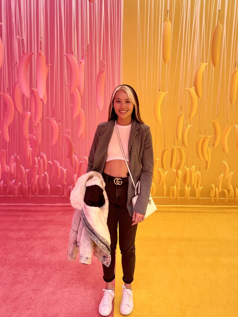 Woman in her 30s in plaid blazer against a colorful pink and yellow banana art wall