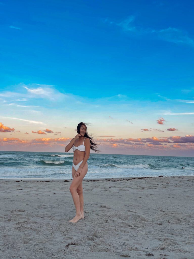 Woman posing in white bikini on Florida beach at sunset with colorful clouds