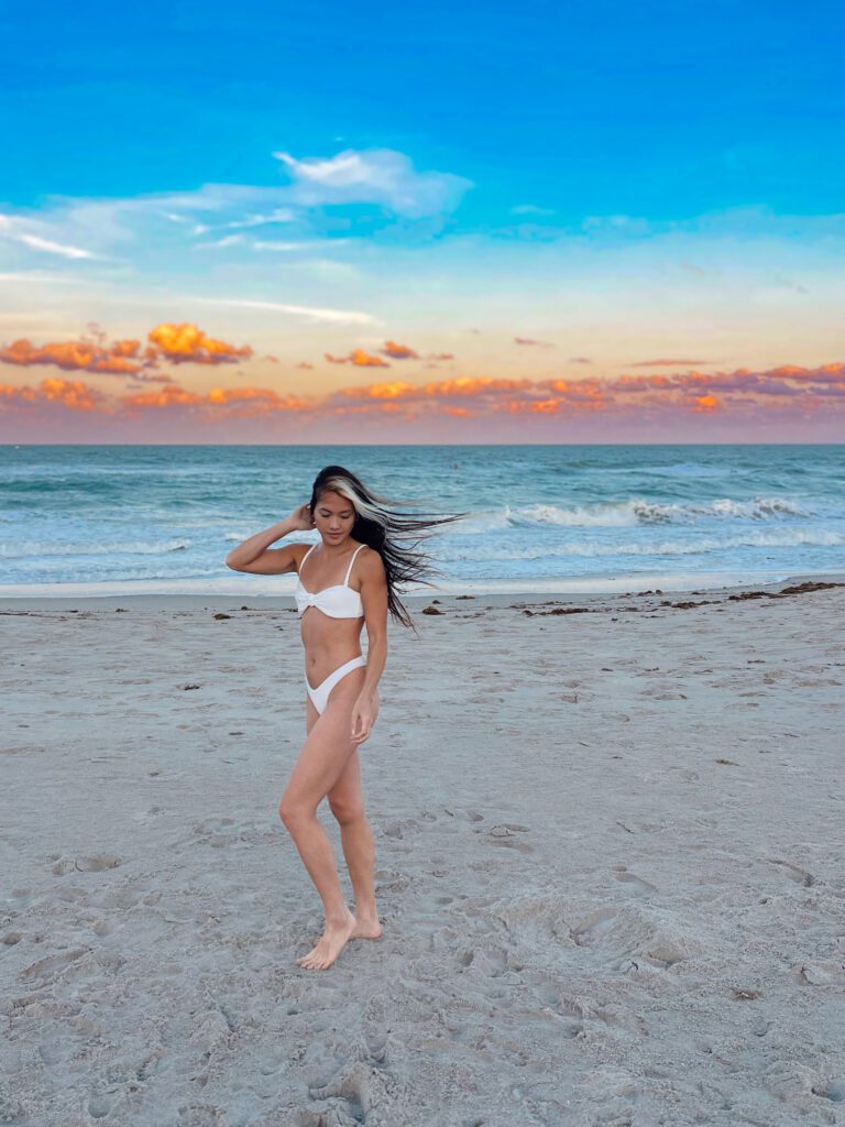 Woman in white bikini on sandy beach with windblown hair at golden sunset
