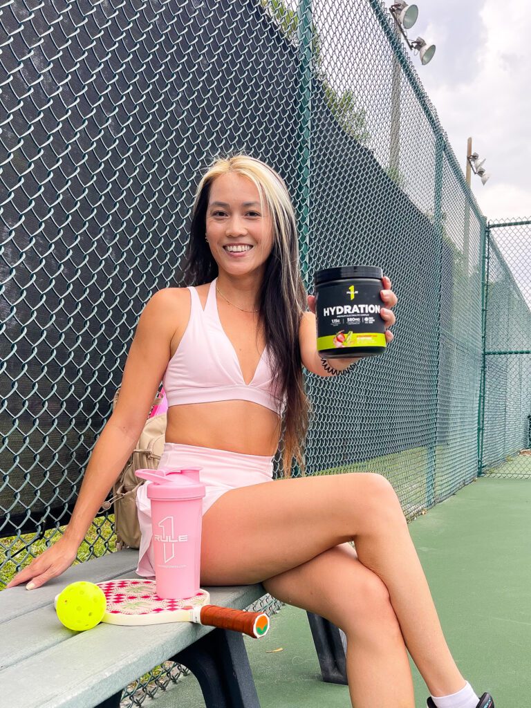 Woman in pink activewear with a Rule One protein tub